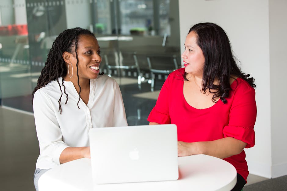pexels-photo-1181724-1181724 Two women in an office discussing work using a laptop, smiling and engaged.